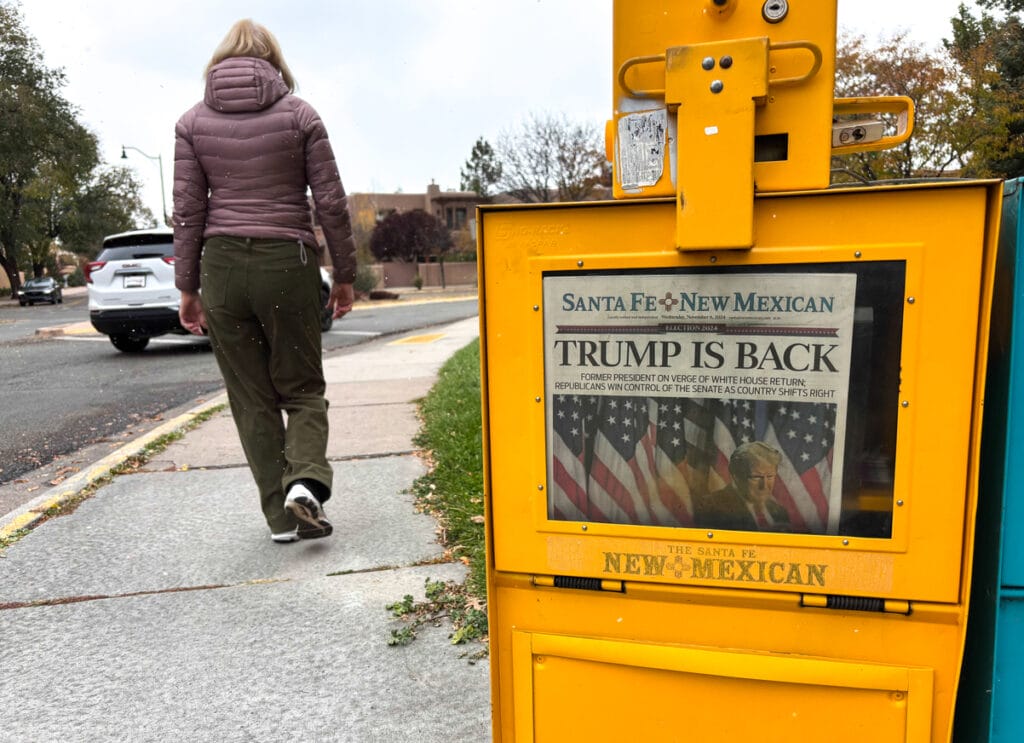 Santa Fe, NM: A woman walks past a Santa Fe New Mexican vending box in downtown Santa Fe, where the headline reads “Trump is Back.”
