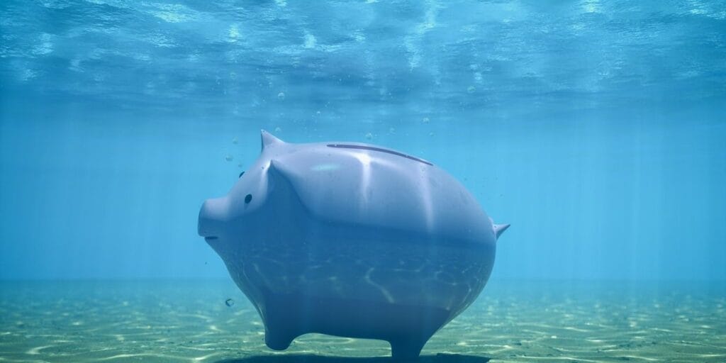 Piggy bank placed underwater on the ocean floor, visualizing economic pressure, debt, or sinking investments.